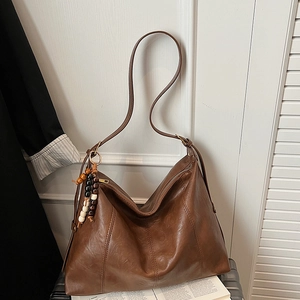 Detail of a brown vintage hobo bag with wooden bead charm on leather surface