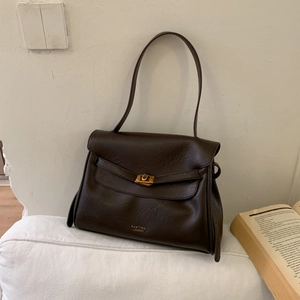Detail of dark brown leather shoulder bag with a gold clasp and logo on a soft cushion