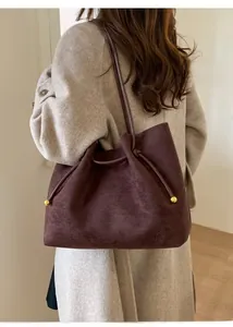 Detail of dark brown suede tote bag with drawstring tassels and gold metal accents