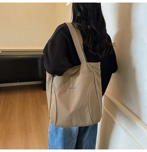 Detailed back view of a khaki canvas tote bag worn on shoulder in a minimalist room