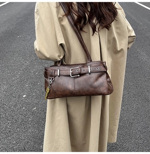 Close-up of vintage brown shoulder bag with metal buckle and key charm on beige coat