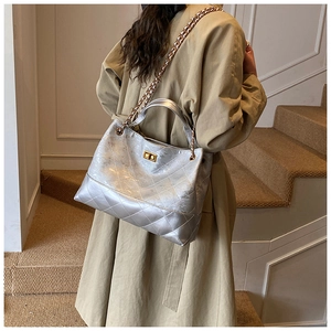 Silver quilted leather tote bag with chain strap and gold lock shown on model's shoulder