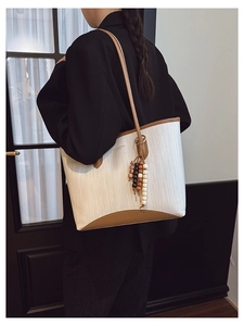 Detail of white woven tote bag with brown leather trim and wooden bead tassel ornament