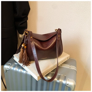 Detail of vintage burgundy leather shoulder bag with decorative tassel and gold hardware