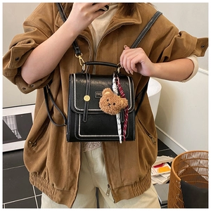 Close-up of black PU leather backpack with white stitching and plush bear charm decoration