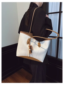 Detail of cream woven tote bag with brown leather trim and bohemian beaded pendant charm