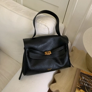 Detail of black tote bag with gold metal clasp and logo on a soft sofa setting