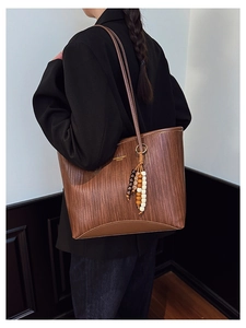 Close-up of brown tote bag with woven texture, beaded tassel, and gold fashion logo