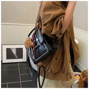 Detail view of black PU leather backpack with white stitching and bear charm accessory