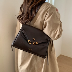 Brown leather tote bag featuring a gold geometric clasp and logo on a khaki trench coat