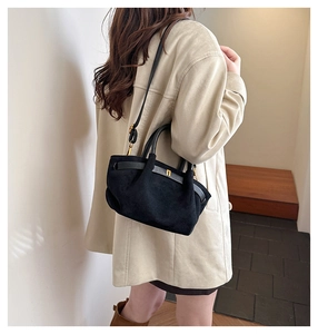 Detail of matte black shoulder bag with gold hardware worn by model in a minimalist setting