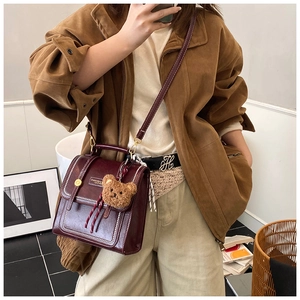Detail view of burgundy retro leather messenger bag with bear charm and metallic buckle