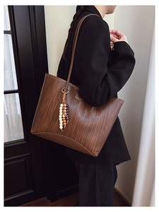 Detail of woven brown tote bag with leather straps and decorative beaded tassel