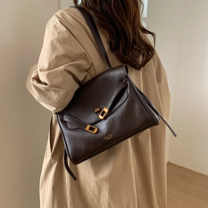 Detail view of the deep brown matte leather tote bag with gold buckle on a beige trench coat