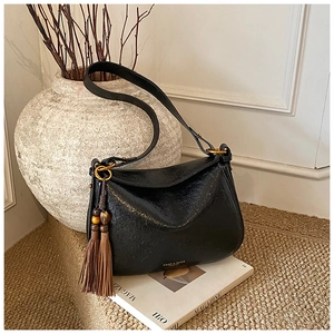 Detail of black glossy leather pillow bag featuring brown tassels and wood bead charm