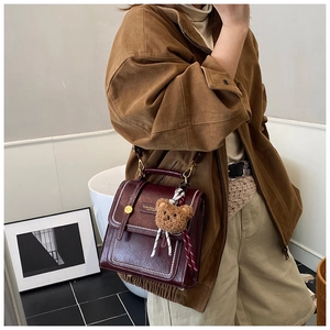 Detail of vintage burgundy leather handbag with top handle and bear charm on a model