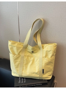 Large pale yellow canvas tote bag with side brand label on a black leather surface
