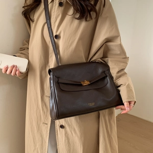 Detail of dark brown leather crossbody bag with gold twist lock and adjustable strap