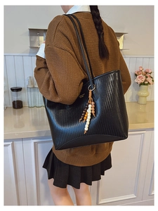 Detail of black woven texture tote bag with ethnic wooden bead tassel in a lifestyle setting