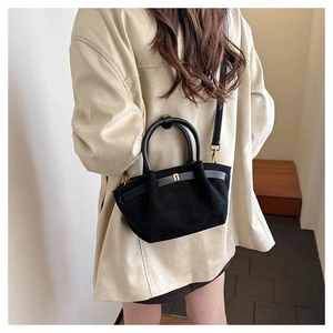 Detail of black matte suede handbag featuring golden metal buckle and winged trapezoid design