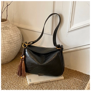 Detail of black vintage shoulder bag with brown tassel and gold hardware on a magazine