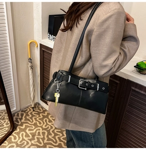 Detail view of black matte leather shoulder bag with buckle and gold key pendant charm