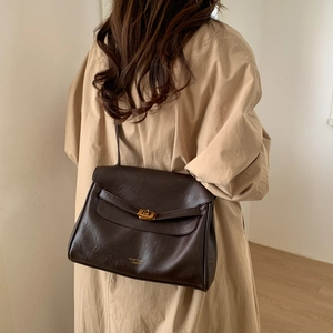 Detail of dark brown leather tote featuring a gold twist lock and adjustable shoulder strap