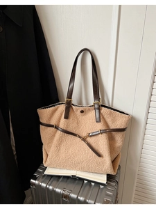 Détail d'un grand sac cabas en peluche beige avec des anses en cuir marron sur une valise