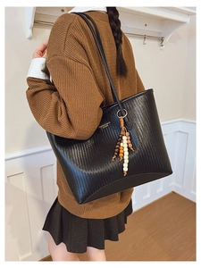 Detail view of black woven tote bag with colorful wooden bead tassel on a model