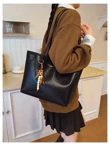 Detail of black woven leather tote bag with vintage texture and ethnic bead charm