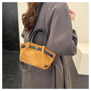 Detail of tan suede handbag with black leather handles and gold metal hardware accents