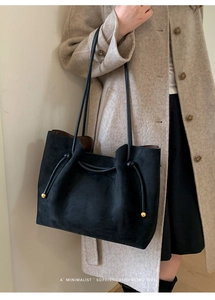 Detail of a black suede tote bag with decorative side knots and gold metal bead accents