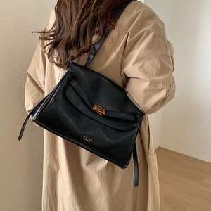 Detail of black faux leather tote with golden metal lock and embossed gold brand lettering