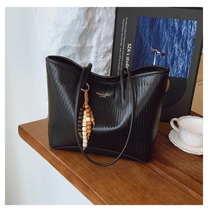 Detail view of black woven tote bag featuring a decorative wooden bead tassel and logo