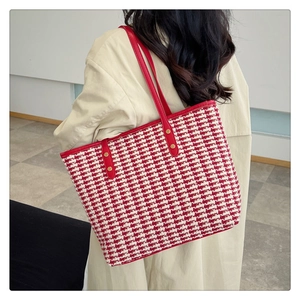 Detail of red houndstooth tote bag with leather straps and metal rivets on model