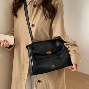 Close-up of minimalist black leather tote with golden clasp and logo on a beige trench coat