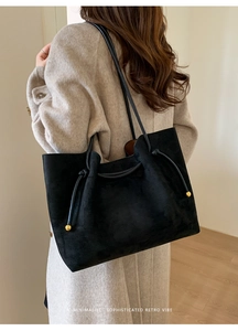 Detail view of black suede tote bag with drawstring and golden bead accents on wool coat