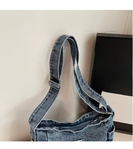 Detail of adjustable long shoulder strap and zipper on washed blue denim crossbody bag