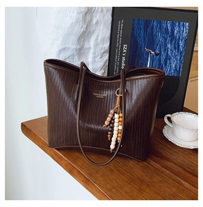 Detailed view of dark brown woven tote bag featuring beaded tassel and logo print