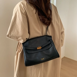Model wearing a black leather tote bag with gold twist lock and brand logo details