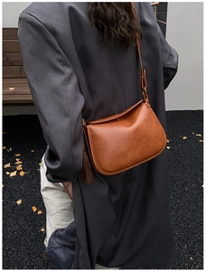 Detail of a brown leather crossbody bag with lychee texture and fringe tassel charm
