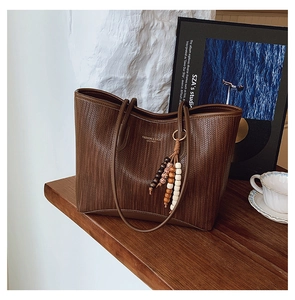 Close-up of dark brown woven tote bag with gold lettering and stylish beaded tassel detail