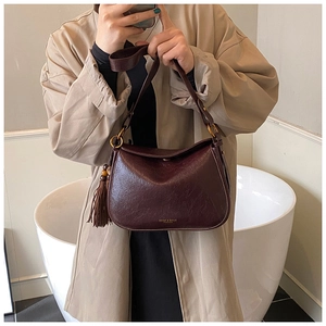 Detail of dark brown leather shoulder bag featuring tassel charm and gold hardware