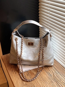 Silver quilted shoulder bag with metal chain strap and turn-lock closure on a wooden desk