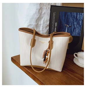 Detail of woven tote bag with brown leather trim and decorative beaded tassel charm