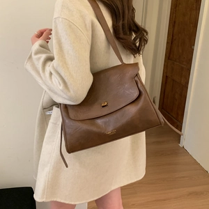 Detailed view of brown leather shoulder bag with gold logo and square metallic buckle clasp
