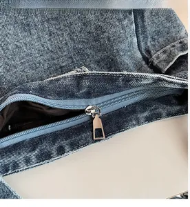 Detailed close-up of the smooth metal zipper and blue denim texture on the shoulder bag