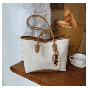 Detail of white herringbone tote bag with brown leather handles and beaded tassel