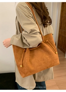 Detail of brown suede tote bag featuring sleek leather straps and gold metal ball accents