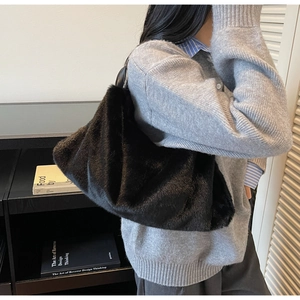 Détail d'un sac à bandoulière en peluche noire plissé porté par un mannequin dans un décor